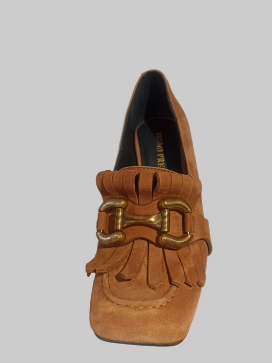 Découvrez l'élégance intemporelle avec cet escarpin Bruno Premi en daim camel. Inspiré des codes de la mode classique, ce modèle allie sophistication et confort avec ses détails raffinés : franges délicates et mors métallique. Confectionné en cuir véritable, il offre une doublure et une semelle intérieure 100% cuir pour un bien-être optimal. Son talon de 7,8 cm et son bout carré affinent la silhouette, tandis que la semelle en caoutchouc assure une stabilité durable. Une pièce incontournable pour sublimer v