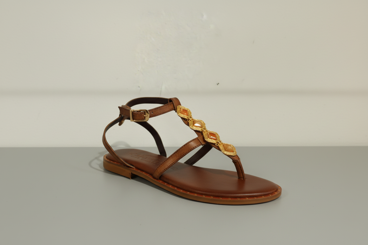 Sandale plate en cuir chocolat ornée de cabochons dorés sur le cou-de-pied. Entièrement en cuir véritable avec première rembourrée pour un confort optimal. Maintien assuré par une sangle tour de cheville ajustable. Petit talon discret pour une allure élégante et intemporelle.