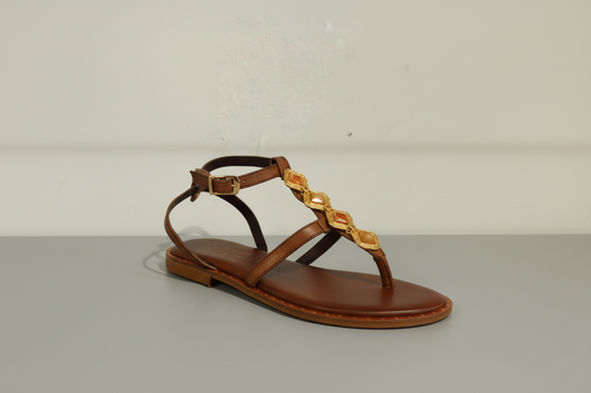 Sandale plate en cuir chocolat ornée de cabochons dorés sur le cou-de-pied. Entièrement en cuir véritable avec première rembourrée pour un confort optimal. Maintien assuré par une sangle tour de cheville ajustable. Petit talon discret pour une allure élégante et intemporelle.