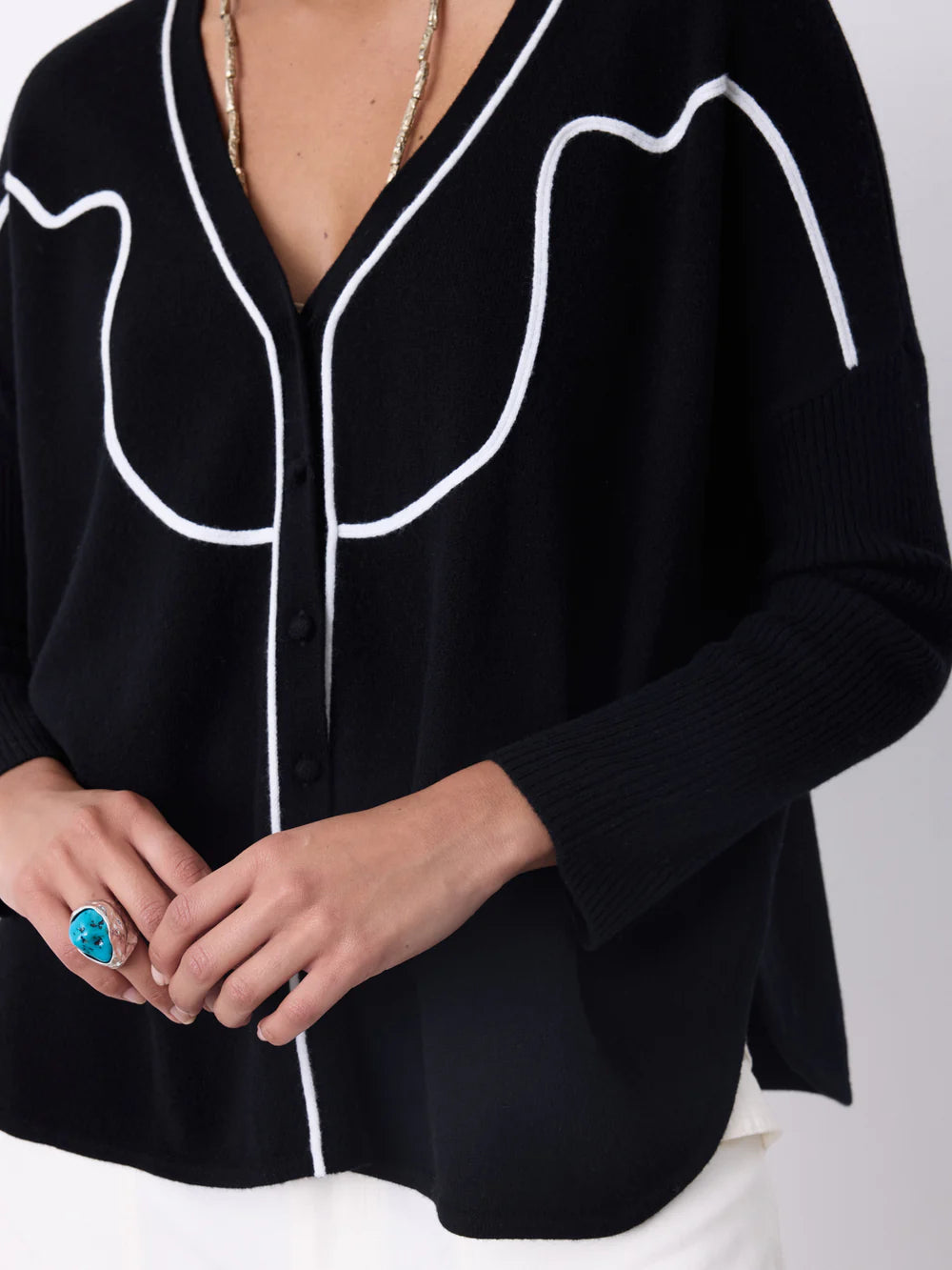 Découvrez le cardigan Bennet de Notshy, un essentiel d'hiver alliant élégance et confort. Sa coupe poncho fluide, ses manches longues côtelées et son col en V dévoilent une silhouette moderne et raffinée. Le fil brodé crème structuré apporte une touche chic et unique, tandis que la fermeture à quatre boutons assure un maintien parfait. Parfait pour vous accompagner tout au long de la saison froide avec style, ce cardigan noir est un incontournable de votre garde-robe.