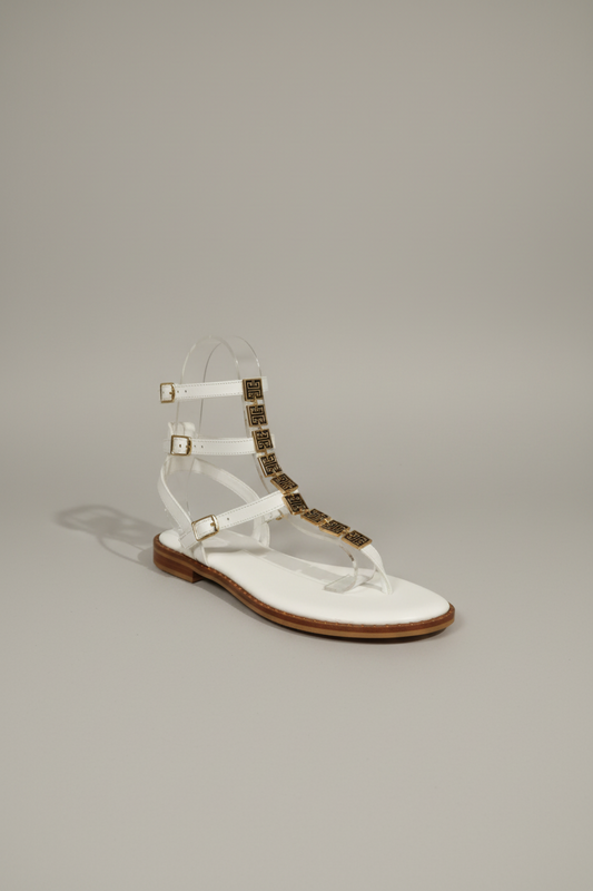 Sandale plate cuir blanche feuille dorée sur cou de pied, petit talon tout cuir, première rembourée pour un confort optimal. Design épuré et élégant, parfait pour l'été.