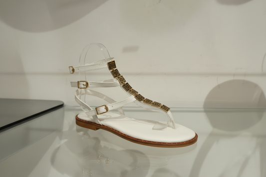 Sandale plate cuir blanche feuille dorée sur cou de pied, petit talon tout cuir, première rembourée pour un confort optimal. Design épuré et élégant, parfait pour l'été.