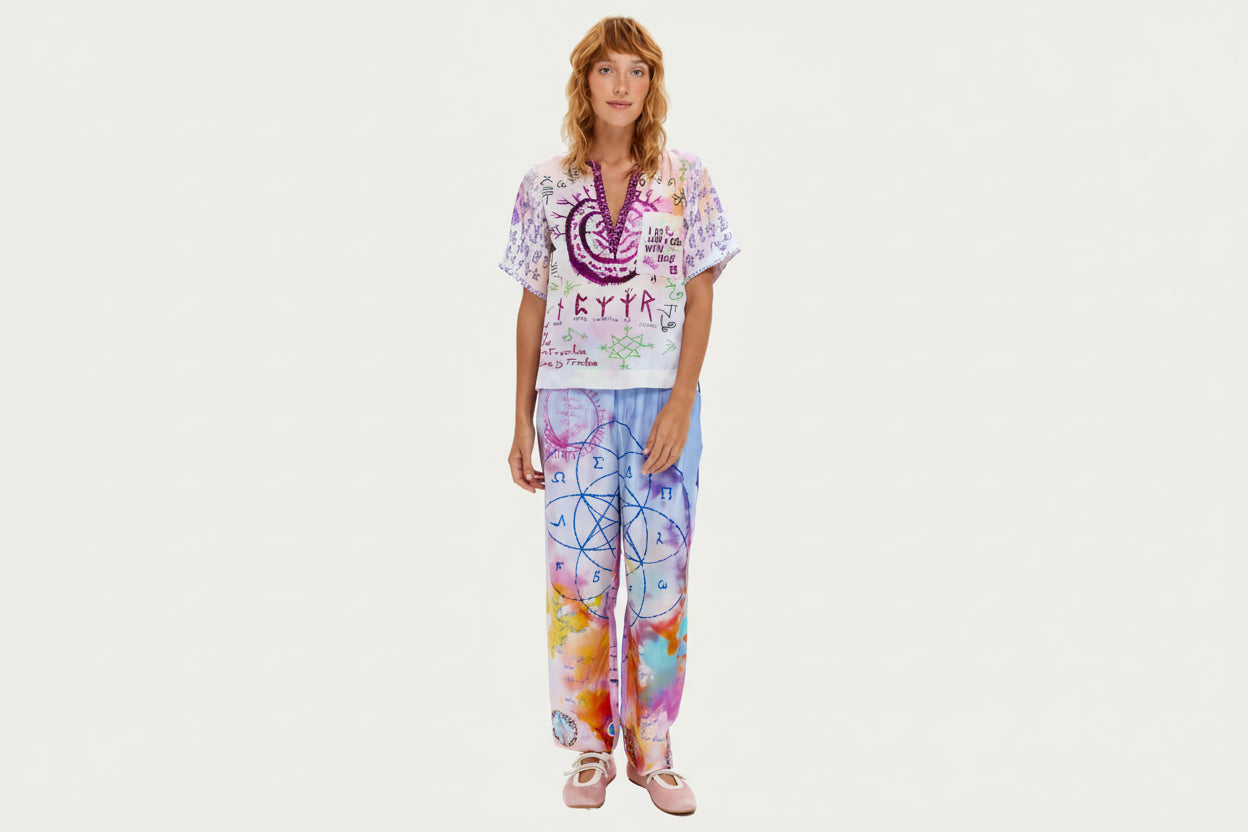 Marchez sur votre chemin spirituel vêtue du pantalon Lydia, orné de mystérieux scripts runiques, de géométrie sacrée et d'affirmations inspirantes. Ce pantalon signature arbore un tie-dye violet et rose avec des symboles dessinés à la main incluant spirales, échelles, cœurs et runes protectrices. La coupe décontractée avec taille élastique offre un confort toute la journée, tandis que des messages significatifs comme « Praying on our love » et des motifs géométriques créent une pièce véritablement unique. C
