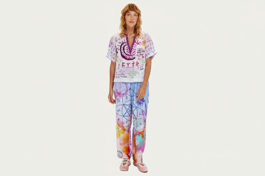 Marchez sur votre chemin spirituel vêtue du pantalon Lydia, orné de mystérieux scripts runiques, de géométrie sacrée et d'affirmations inspirantes. Ce pantalon signature arbore un tie-dye violet et rose avec des symboles dessinés à la main incluant spirales, échelles, cœurs et runes protectrices. La coupe décontractée avec taille élastique offre un confort toute la journée, tandis que des messages significatifs comme « Praying on our love » et des motifs géométriques créent une pièce véritablement unique. C