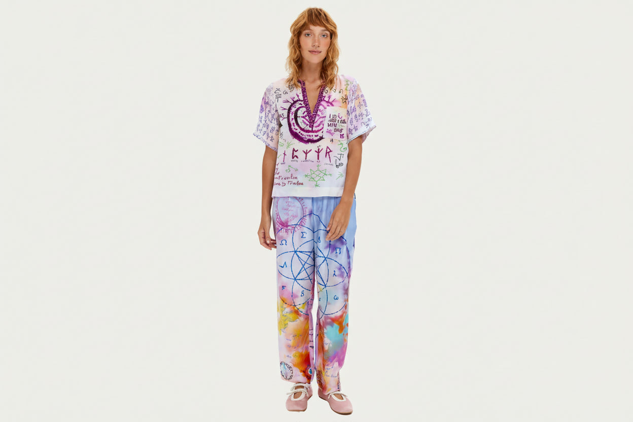 Marchez sur votre chemin spirituel vêtue du pantalon Lydia, orné de mystérieux scripts runiques, de géométrie sacrée et d'affirmations inspirantes. Ce pantalon signature arbore un tie-dye violet et rose avec des symboles dessinés à la main incluant spirales, échelles, cœurs et runes protectrices. La coupe décontractée avec taille élastique offre un confort toute la journée, tandis que des messages significatifs comme « Praying on our love » et des motifs géométriques créent une pièce véritablement unique. C