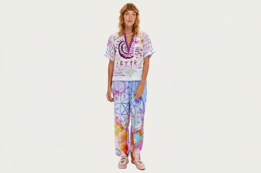 Marchez sur votre chemin spirituel vêtue du pantalon Lydia, orné de mystérieux scripts runiques, de géométrie sacrée et d'affirmations inspirantes. Ce pantalon signature arbore un tie-dye violet et rose avec des symboles dessinés à la main incluant spirales, échelles, cœurs et runes protectrices. La coupe décontractée avec taille élastique offre un confort toute la journée, tandis que des messages significatifs comme « Praying on our love » et des motifs géométriques créent une pièce véritablement unique. C
