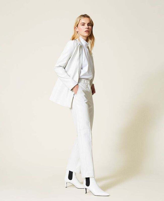 Femme portant un twinset pantalon simili blanc à coupe droite avec veste assortie et bottines blanches à talon.